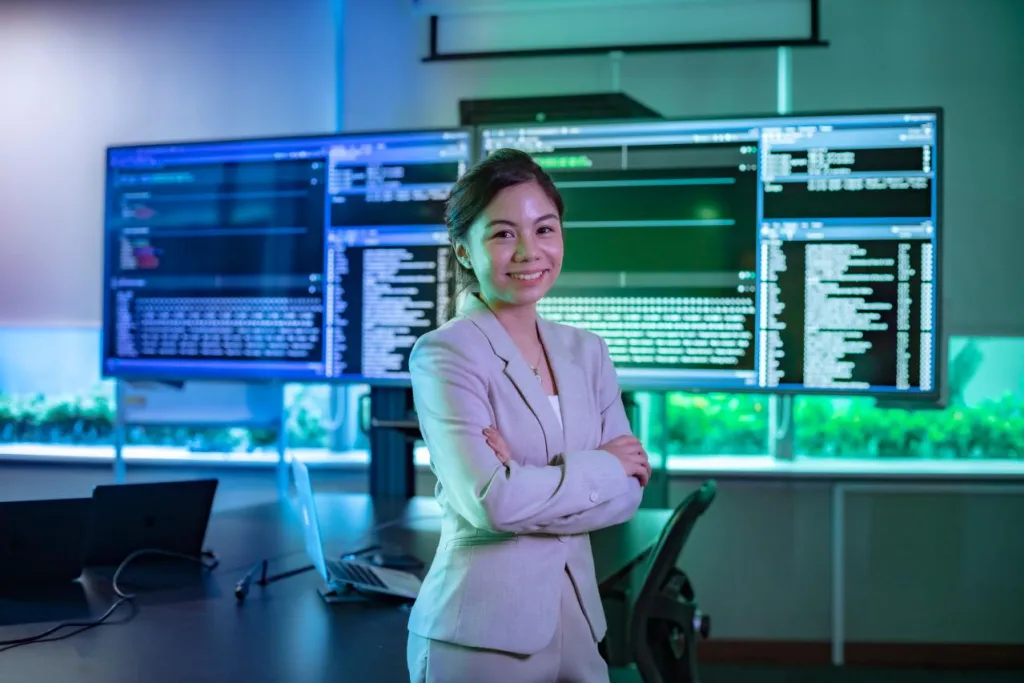 Research - Digital Transformation | Student standing confidently in front of 2 monitors.